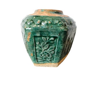May include: A small, green, octagonal ceramic vase with raised floral designs. The vase has a worn, aged appearance.