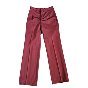 May include: Burgundy-colored, high-waisted trousers with a classic, tailored design. The pants feature a button and zipper closure, belt loops, and a wide-leg silhouette. The fabric appears to be a smooth, woven material, suitable for a polished look.