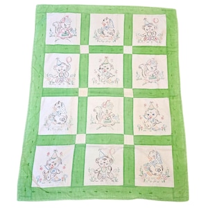 May include: A green and white baby quilt with embroidered images of animals wearing party hats. The quilt is made of a soft, cotton fabric and is perfect for a baby's nursery.