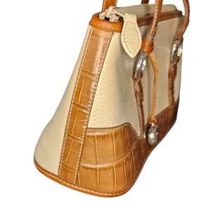 May include: Cream-colored handbag with brown crocodile-textured leather accents. The bag features a structured design with a top handle and silver-tone hardware. The bag's trim and handle are made of smooth brown leather.