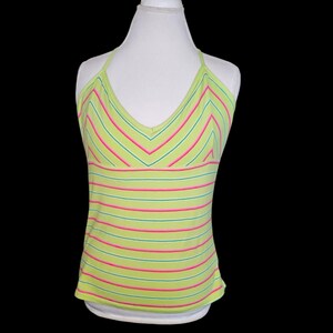 May include: A lime green halter top with horizontal pink and teal stripes. The top has a V-neck and is displayed on a white mannequin. The top is sleeveless and has a fitted silhouette.