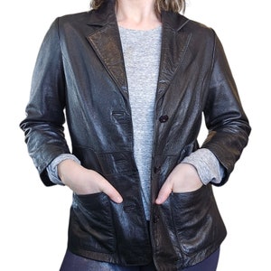 May include: A black leather jacket with a button-up front and two flap pockets. The jacket has a classic style and is made of a soft, supple leather.
