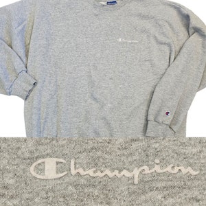 May include: Gray Champion sweatshirt with a white embroidered logo on the front and a small Champion logo patch on the left sleeve.