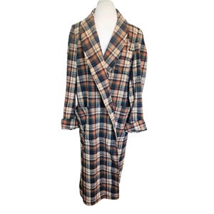 May include: A long-length robe featuring a plaid pattern in shades of dark green, orange, and cream. The garment includes a wide shawl collar, long sleeves with folded cuffs, and two large patch pockets on the front, providing a structured silhouette.