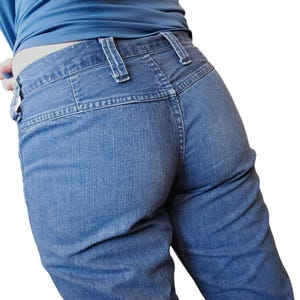 May include: Close-up of blue denim jeans. The jeans have a high waist and a classic five-pocket design. The denim fabric has a medium wash and visible stitching details. The jeans are worn with a blue top.