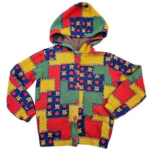 May include: A colorful hooded cardigan with a patchwork design featuring red, yellow, blue, and green squares. The cardigan has a button closure and is decorated with small red hearts and yellow flowers.