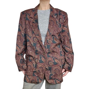 May include: A paisley patterned blazer with a dark green background and red, brown, and gold accents. The blazer has a single button closure and long sleeves.