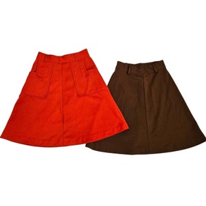 May include: Two skirts, one red and one brown. The red skirt has two large pockets on the front. The brown skirt is a simple A-line style.