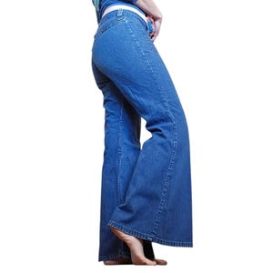May include: Light blue denim bell-bottom jeans. The jeans have a classic five-pocket design and a high waist. The legs flare out dramatically from the knee down, creating a wide, bell-bottom silhouette. The jeans are made of a medium-weight denim fabric.