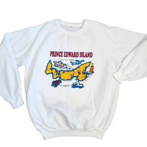 May include: White sweatshirt with a colorful graphic of Prince Edward Island, Canada. The graphic includes a map of the island, a boat, a lobster, and a swimmer.