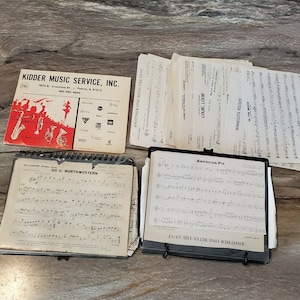 May include: A collection of sheet music for various songs, including "American Pie", "Go U. Northwestern", "Another One Bites the Dust", "Louie, Louie", "Minnesota Rouser", "In the Mood", and "Land of a Thousand Dances".