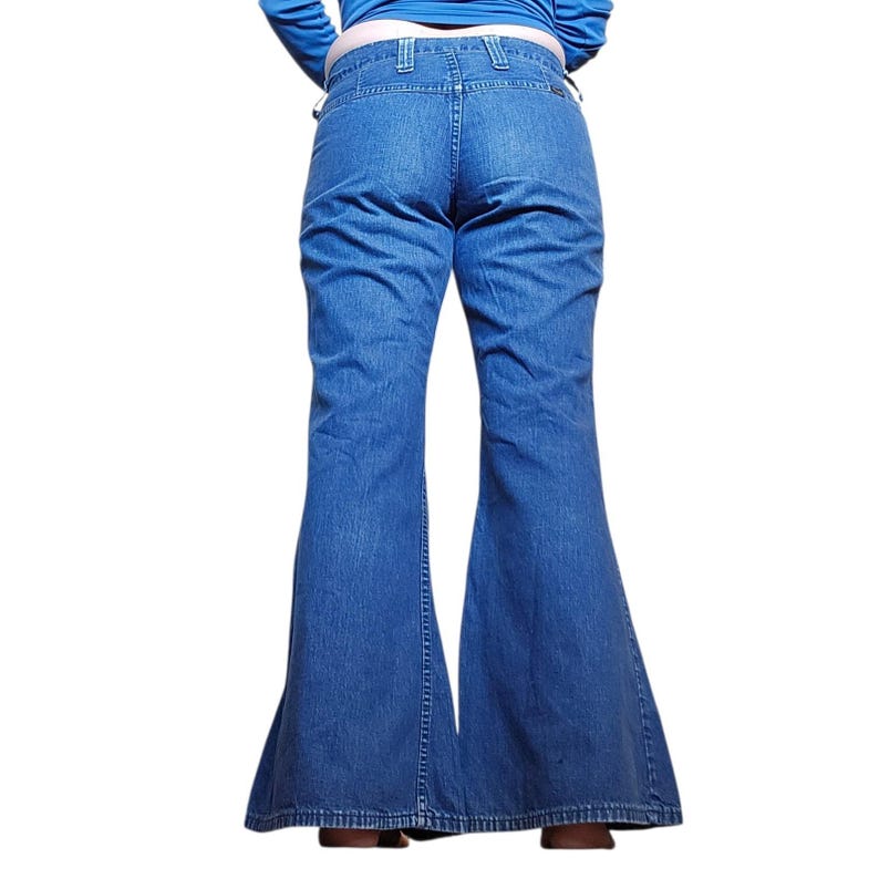 May include: Blue denim bell-bottom jeans. The jeans have a high waist and a flared leg design. The back view shows the pockets and the stitching details. The jeans are made of a medium-wash denim fabric.