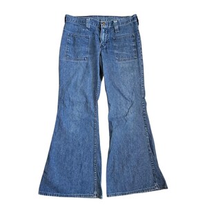 May include: Light blue denim jeans with a flared leg design. The jeans have two front pockets and a button and zip closure. The denim is a medium wash, and the jeans appear to be vintage or retro style.
