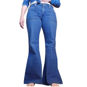 May include: Blue denim flared jeans with two front pockets. The jeans have a classic five-pocket design and a high waist. The denim is a medium wash, and the jeans flare out from the knee down.