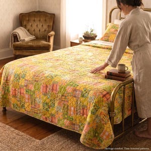 May include: A patchwork quilt featuring a variety of yellow, orange, and green fabric squares with assorted plaid, floral, and geometric patterns. The quilt is draped over a metal bed frame, with two stacked books and a mug resting on the surface.