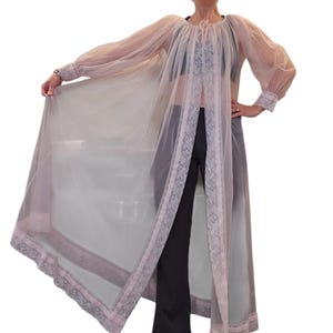 May include: A sheer, light pink vintage robe with long sleeves and a delicate lace trim. The robe is open in the front and has a flowing, elegant design. The sleeves are gathered at the wrists, and the neckline is gathered with a pink tie.