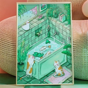 Op de afbeelding: Een rechthoekige kunstdruk met een badkamer met groene tegels, een badkuip gevuld met water, twee koivissen en een kleine kikker. Er zijn twee lapjeskatten aanwezig, één staat bij het bad en één zit op een matje. Kamerplanten en een eend zijn zichtbaar.