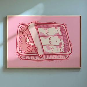 Op de afbeelding: Een ingelijste roze kunstprint met een gestileerde illustratie van drie katvormige sushirollen in een roze bakje. Op het bakje staat het woord "SA". Het kunstwerk staat tegen een roze achtergrond.