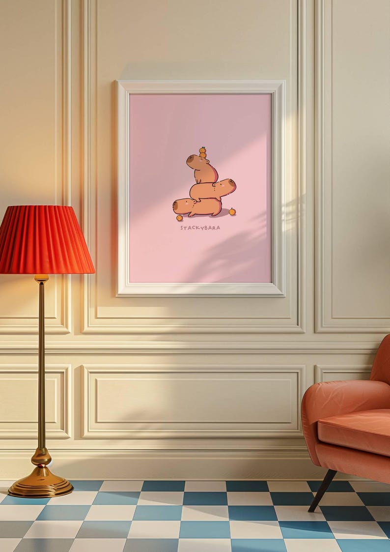 May include: A framed art print showing a stack of cartoon capybaras on a pink backdrop. The capybaras are stacked, with a small carrot on top. The text "STACKYBARA" is printed below the capybaras.