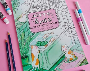 May include: A coloring book titled Kitty & Meg Colouring Book Illustrated by T. Fox featuring a line art illustration of two cats and a duck in a bathroom with a bathtub, surrounded by two paint tubes, two markers, and three watercolor pencils.