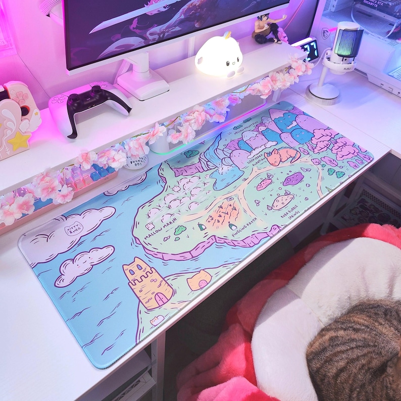 Puede incluir: Una alfombrilla de escritorio rectangular con un mapa ilustrado colorido en tonos pastel de azul, rosa y verde. El dise&ntilde;o incluye paisajes caprichosos etiquetados como Mallow Marsh, Pingling Patch y Boba Bubble Springs, junto con un castillo de arena.