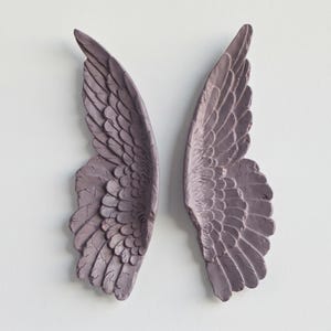Peut inclure: Deux ailes d'ange murales assorties, de couleur mauve. Les ailes pr&eacute;sentent des motifs de plumes textur&eacute;s et d&eacute;taill&eacute;s, sur un fond blanc uni. Les ailes sont un objet d&eacute;coratif.