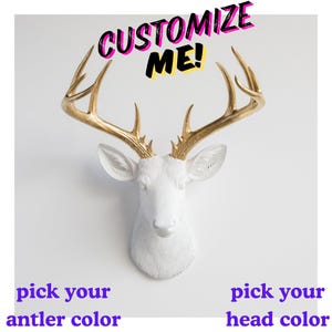 以下が含まれることがあります： 金色の角を持つ白い鹿の頭の壁掛け。鹿の頭の上には「CUSTOMIZE ME！」という文字があります。鹿の頭の下には「pick your antler color」と「pick your head color」という言葉があります。