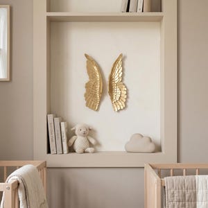 A cozy nursery with a shelf displaying a stuffed lamb, a cloud, and two golden winged sculptures. The room has a neutral color scheme and a minimalist design.
