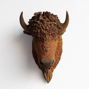 Puede incluir: Escultura detallada de una cabeza de bisonte de estilo rústico. La escultura presenta un acabado texturizado, marrón y naranja, con cuernos prominentes y una textura de pelaje detallada. La cabeza de bisonte está montada sobre un fondo blanco.