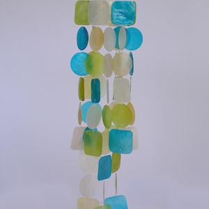 May include: A colorful wind chime with a wooden top and strands of iridescent, square, and circular shapes in shades of blue, green, and white. The shapes are strung together, creating a decorative hanging ornament.