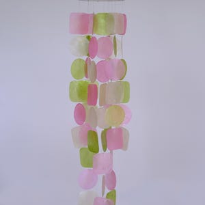 Peut inclure: Un carillon éolien décoratif avec un anneau en bois en haut et des brins de formes translucides colorées. Les formes comprennent des carrés, des cercles et des rectangles dans des tons de rose, de vert et de blanc.