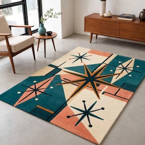 Op de afbeelding: Een rechthoekig vloerkleed met een geometrisch patroon van blauwgroene, crèmekleurige en koraalkleurige vormen. Het ontwerp bevat meerdere stervormige motieven met dunne zwarte lijnen en cirkelvormige accenten op het oppervlak van het kleed.