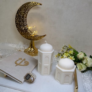 Islamisches Ramadan Kerzen Set in Cremeweiß mit zwei architektonischen Moschee-Kerzen und Kuppeldesign. Fein gearbeitete Fensterornamente, goldener Halbmond mit warmem Licht im Hintergrund. Perfekte Deko für Ramadan, Iftar Tisch, Gebetsraum oder als edles muslimisches Geschenk zu Eid.