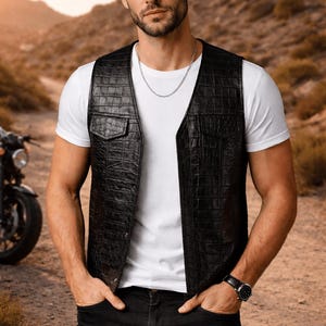 Peut inclure: Gilet en cuir noir avec un motif texturé, porté sur un t-shirt blanc et un jean noir. Un collier chaîne argenté et une montre noire complètent le look. Une moto est partiellement visible en arrière-plan.