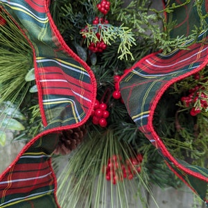 May include: A Christmas wreath with green pine branches, red berries, and a plaid ribbon with red, green, and white stripes.