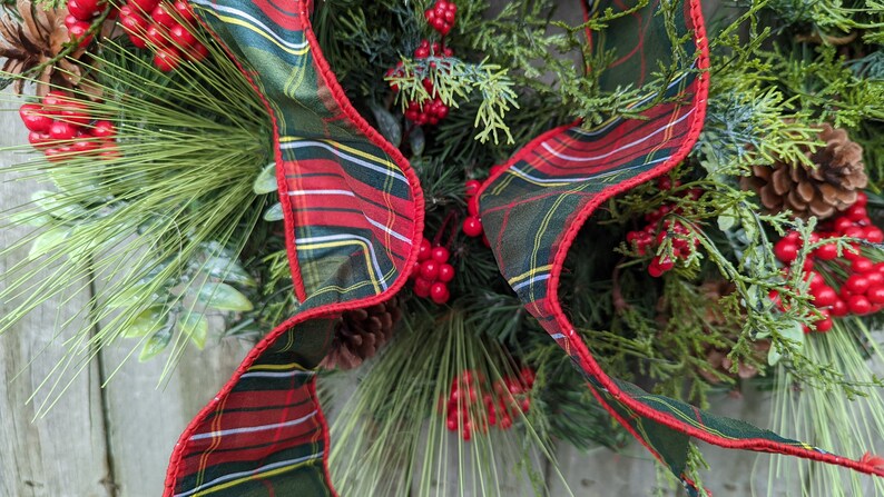 May include: A Christmas wreath with green pine branches, red berries, and a plaid ribbon with red, green, and white stripes.