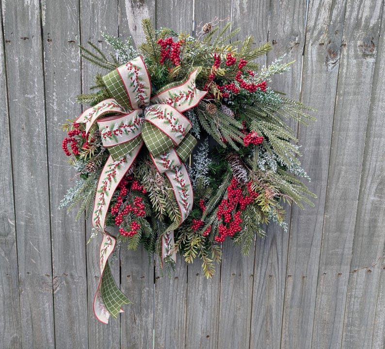 May include: A festive Christmas wreath with a mix of evergreen branches, red berries, and a large bow. The bow features a green and white checkered pattern with a red berry design. The wreath is displayed against a weathered wooden fence.