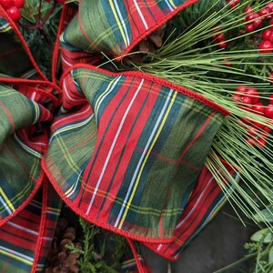 May include: A green and red plaid ribbon with a red trim, tied into a bow. The ribbon is decorated with sprigs of green pine and red berries.
