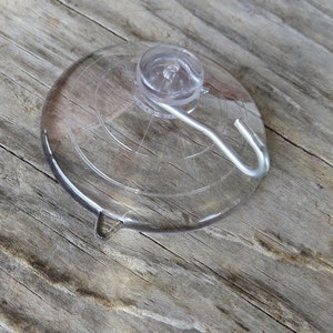 May include: A clear suction cup hook with a metal hook. The suction cup is round and has a textured surface. The hook is silver and has a simple design.