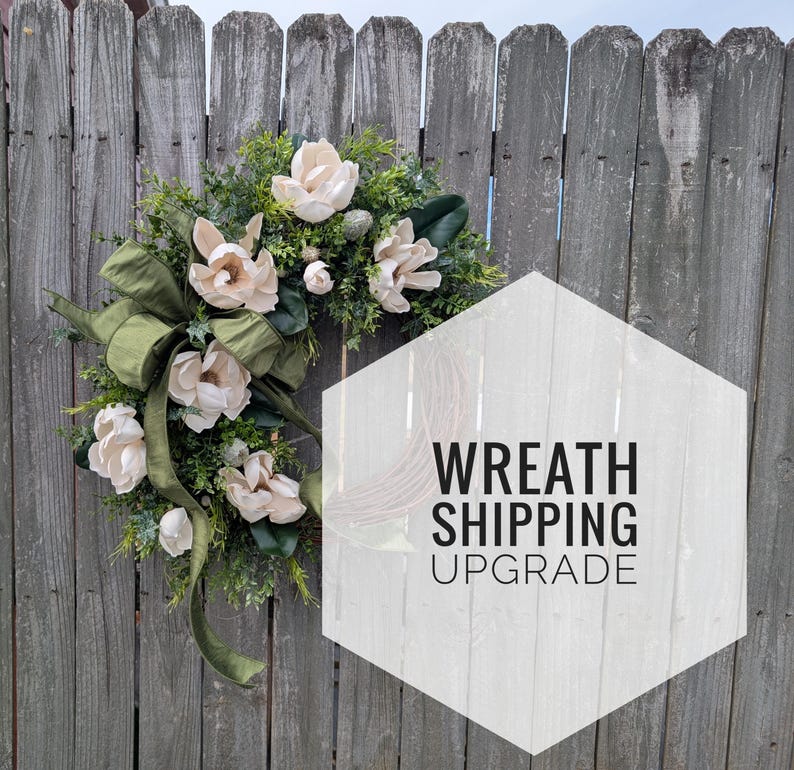 Pu&ograve; includere: Una ghirlanda decorativa con fiori di magnolia color crema, fogliame verde e un grande fiocco di nastro verde oliva. Un sovrapposizione esagonale bianca sulla destra contiene il testo nero WREATH SHIPPING UPGRADE in carattere sans-serif.