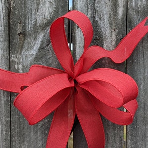 May include: A red ribbon bow tied around a wooden fence post.