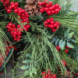 May include: A close-up of a Christmas wreath with red berries, pine needles, and a plaid ribbon.