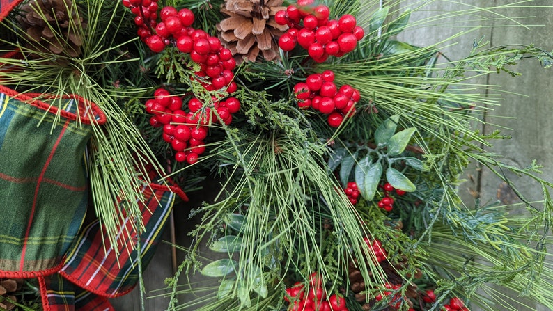 May include: A close-up of a Christmas wreath with red berries, pine needles, and a plaid ribbon.
