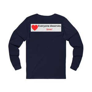 Back view of a navy blue long-sleeve t-shirt showing a white rectangular graphic near the collar with a red heart and the text Everyone deserves love!.