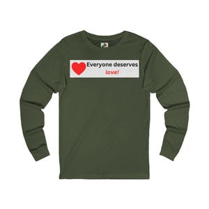 Front view of an olive green long-sleeve t-shirt with a white rectangular chest graphic containing a red heart and the text Everyone deserves love!.