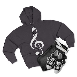 A dark grey zippered hoodie with a large white treble clef graphic on the front, paired with folded dark denim jeans and black and white canvas sneakers.