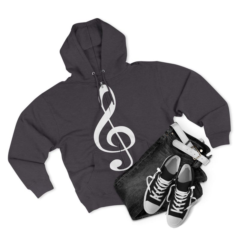 A dark grey zippered hoodie with a large white treble clef graphic on the front, paired with folded dark denim jeans and black and white canvas sneakers.