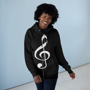 A smiling woman wearing a black zip-up hoodie featuring a large white treble clef graphic.