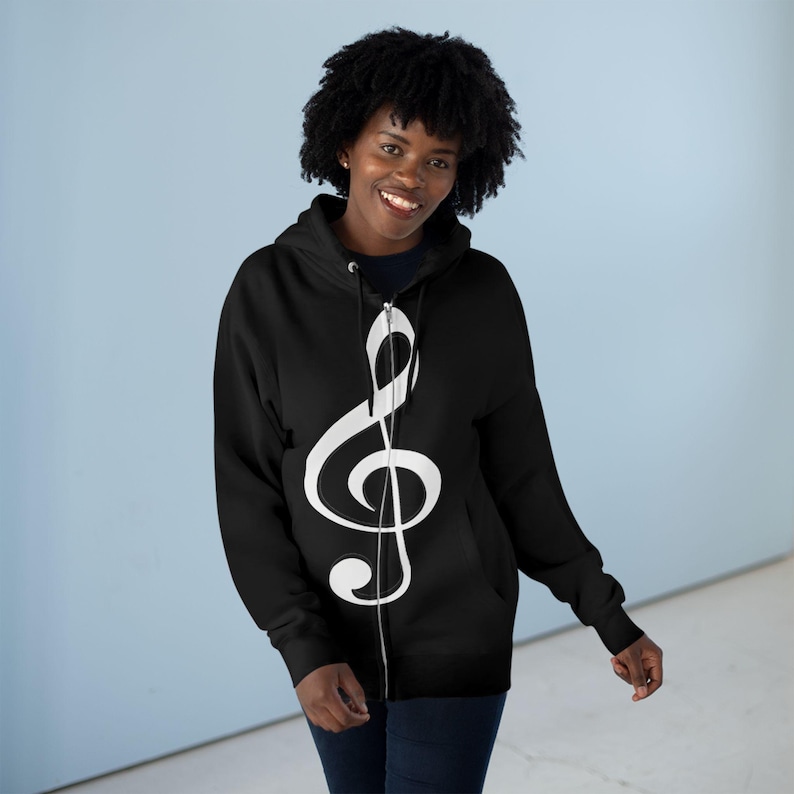 A smiling woman wearing a black zip-up hoodie featuring a large white treble clef graphic.