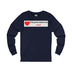 Front view of a navy blue long-sleeve t-shirt with a white rectangular graphic on the chest that displays a red heart and the text Everyone deserves love!.